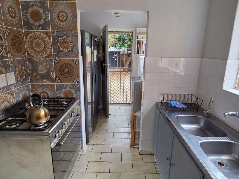 Functional kitchen featuring a gas stove, stainless steel double sink, and decorative tiled splashback with direct access to the rear exterior.