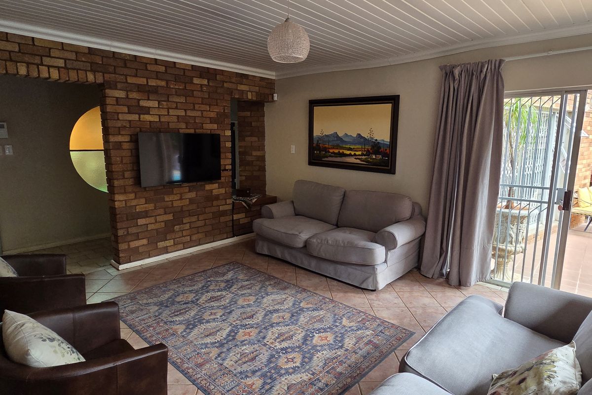 A comfortable living room featuring an exposed brick feature wall, tiled flooring, and direct access to an outdoor patio area through sliding glass doors.