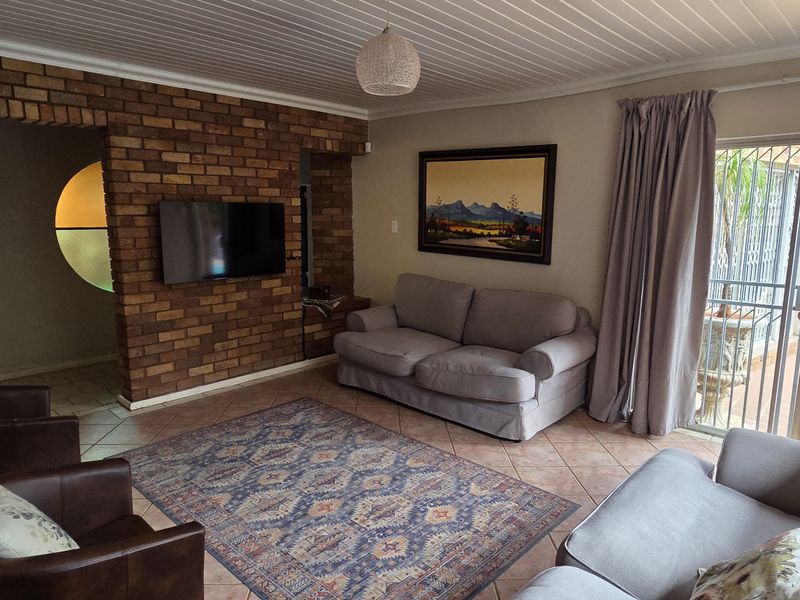 A comfortable living room featuring an exposed brick feature wall, tiled flooring, and direct access to an outdoor patio area through sliding glass doors.