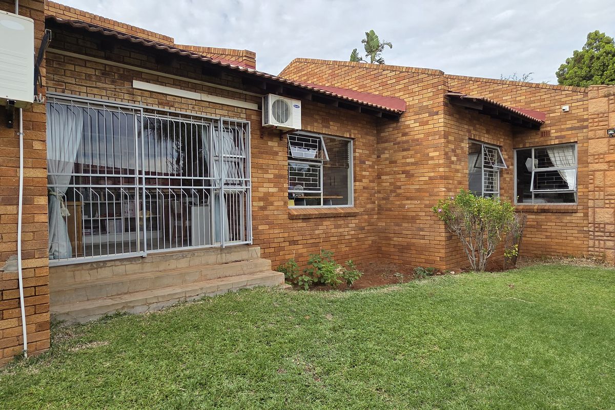 Rear view of a face brick house featuring a lawn, security gates on windows, and installed air conditioning units.