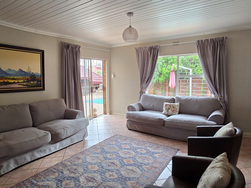 A comfortable living room featuring tiled floors, a tongue and groove ceiling, and direct access to the outdoor pool area through a sliding glass door.