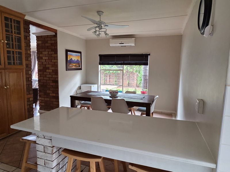 Open-plan living and dining area featuring a breakfast bar, brick feature walls, tiled flooring, and split-system air conditioning.