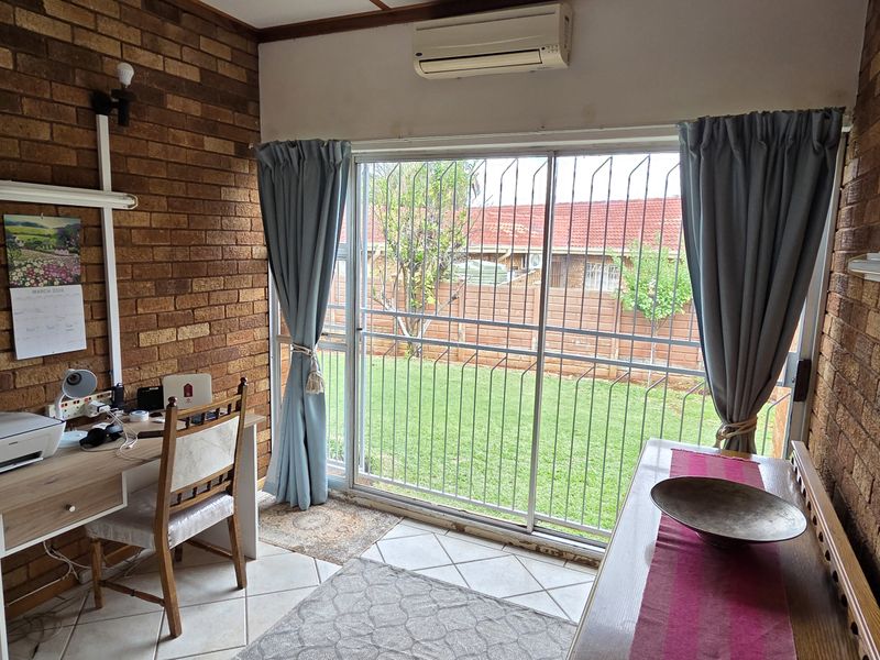 A home office featuring exposed brick walls, tiled flooring, and a sliding glass door with security gate providing access to the garden.