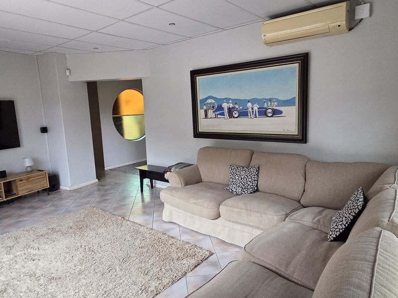 Spacious living room featuring tiled flooring, recessed ceiling lighting, and a wall-mounted split-system air conditioner, with a unique circular window feature.