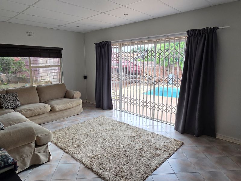 A living room featuring tiled flooring, a drop ceiling with recessed lighting, and a sliding glass door with a security gate leading to the pool area.