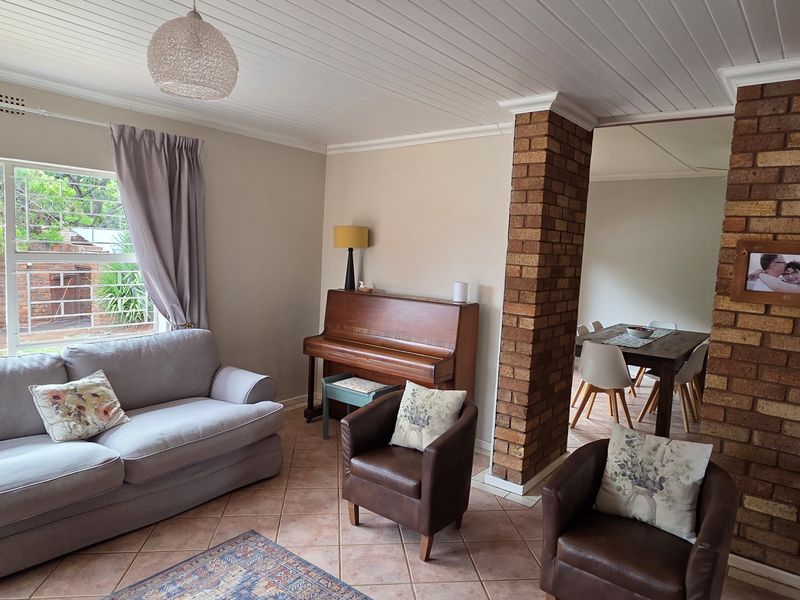 A living room featuring exposed brick accents, tiled flooring, and a tongue and groove ceiling, with a view towards the outdoor area.