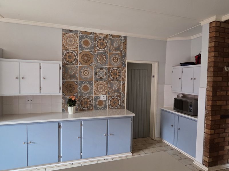 Kitchen area featuring built-in cabinetry, a decorative tiled splashback, and a rustic exposed brick pillar, offering a functional layout with potential for modernization.
