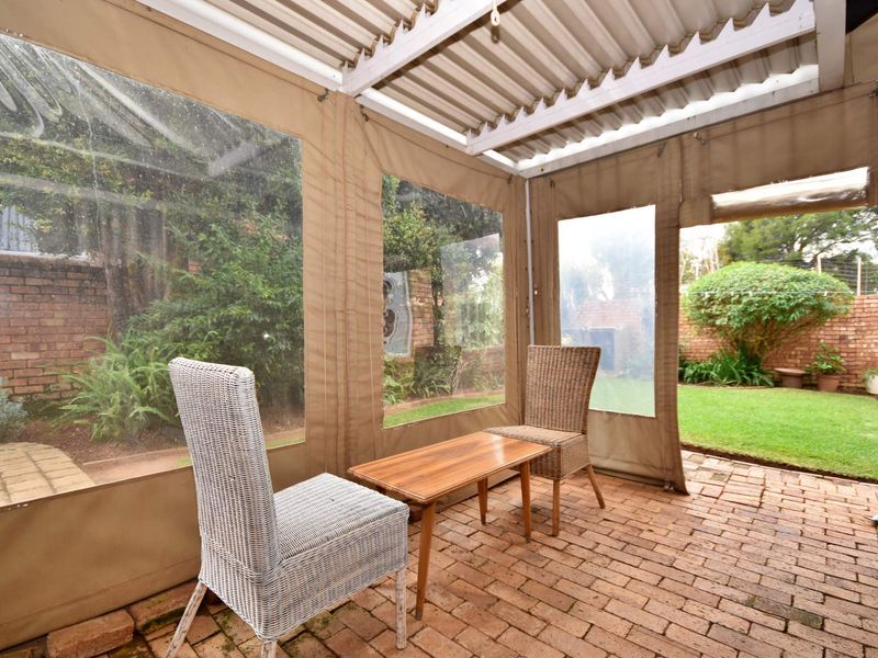 Covered patio area featuring brick paving and roll-up canvas blinds, providing a sheltered outdoor space overlooking the garden.