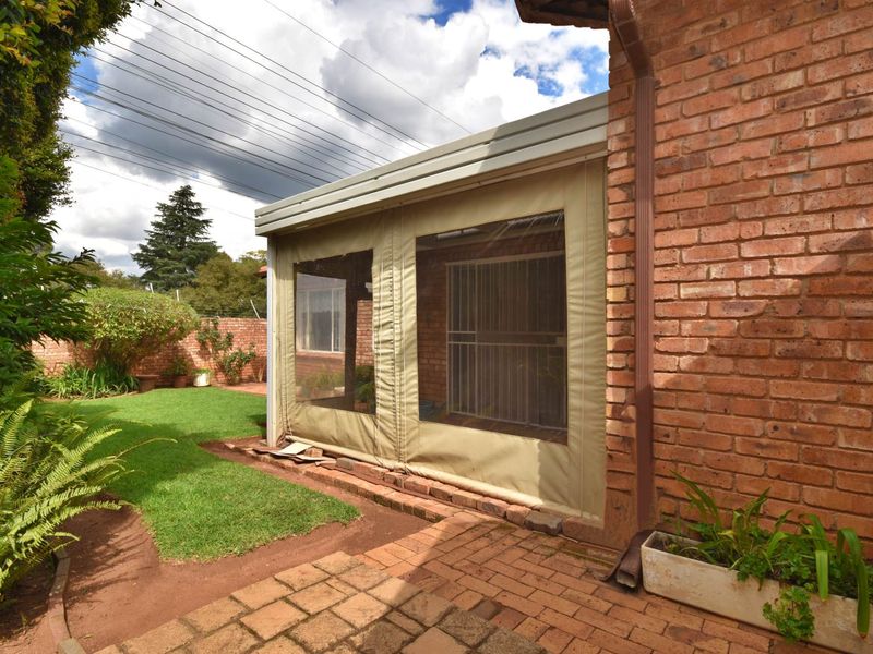 A covered patio area featuring brick construction and protective canvas enclosures, overlooking a private garden space with paved flooring.