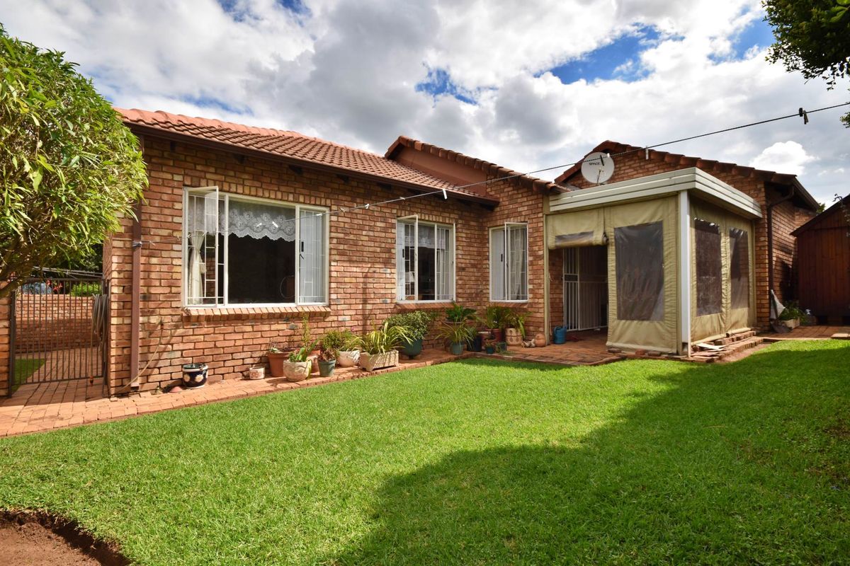 Rear view of a face-brick townhouse featuring a well-maintained lawn and an enclosed patio area with a tiled roof.