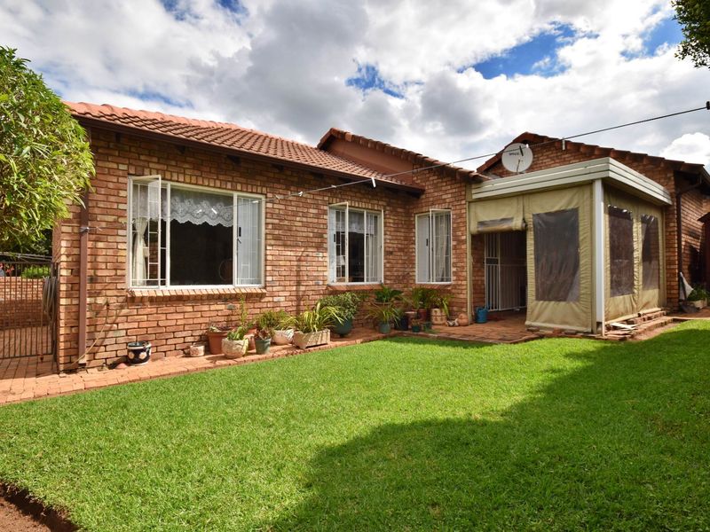 Rear view of a face-brick townhouse featuring a well-maintained lawn and an enclosed patio area with a tiled roof.