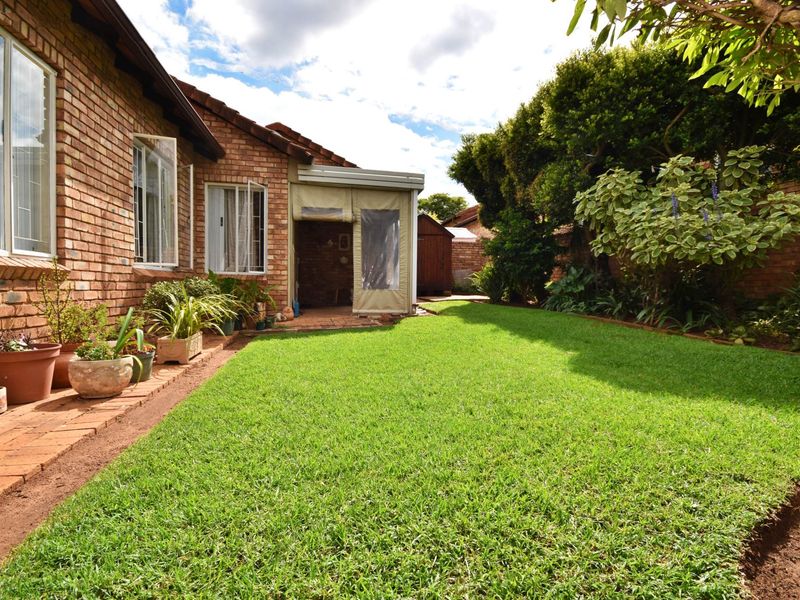 A well-maintained rear garden featuring a lush green lawn, brick exterior facade, and a covered patio area.