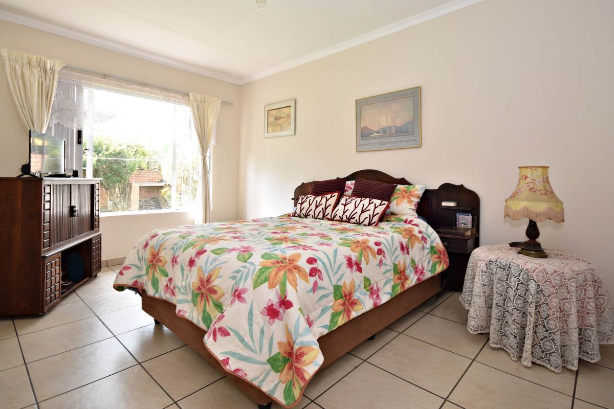 A well-lit bedroom featuring neutral walls, tiled flooring, and a large window providing natural light.