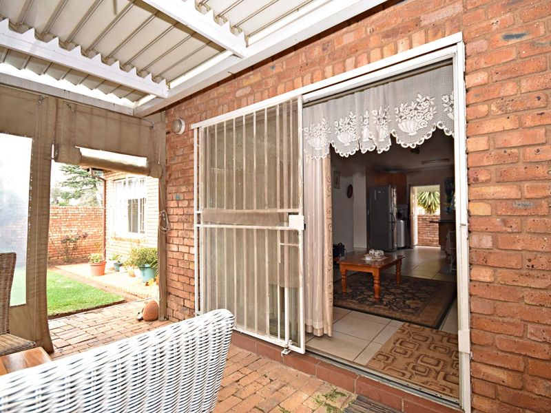 Covered brick patio area with sliding door access to the interior, featuring paved flooring and a corrugated roof structure.