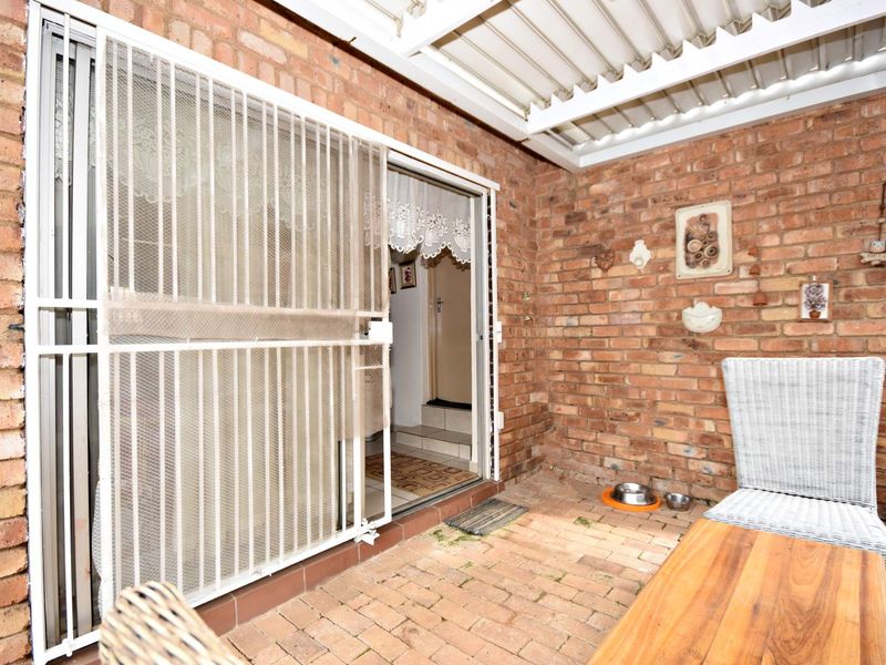 A covered patio area featuring exposed brick walls, brick paver flooring, and a sliding security gate providing access to the interior.