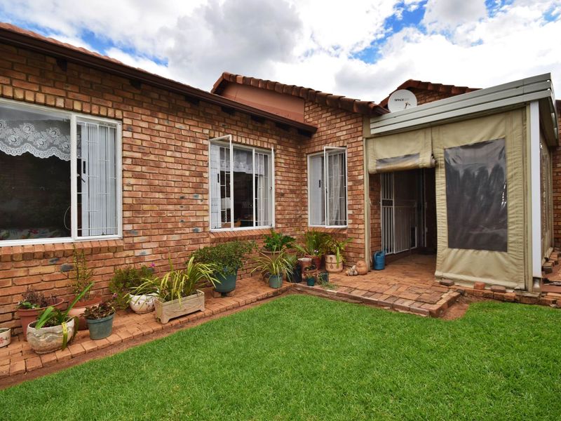 Rear view of the townhouse featuring a face brick facade, a small lawn, and a covered patio area with a canvas enclosure.