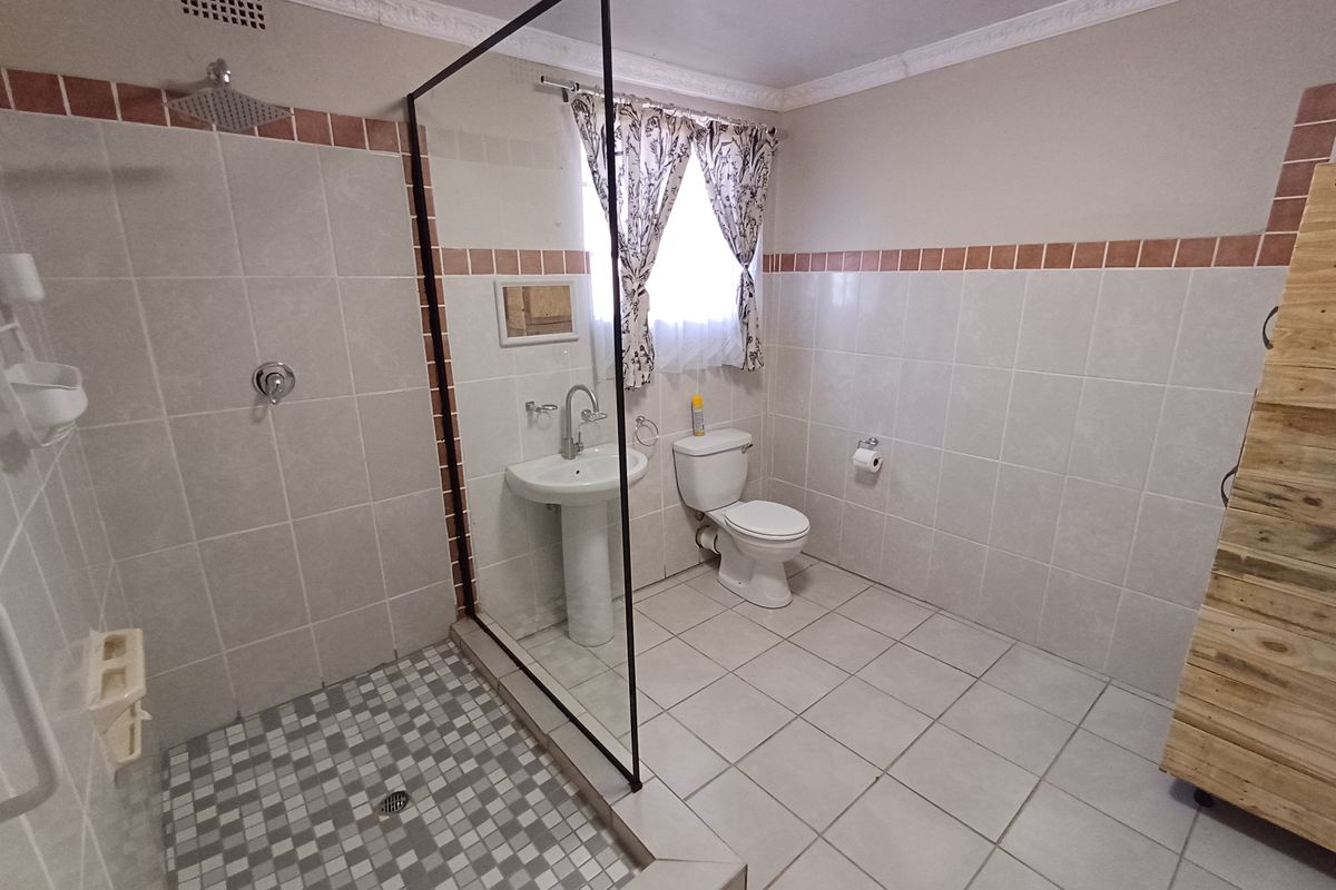 A functional bathroom featuring a walk-in shower with a glass screen, pedestal basin, and toilet, finished with neutral wall and floor tiling.