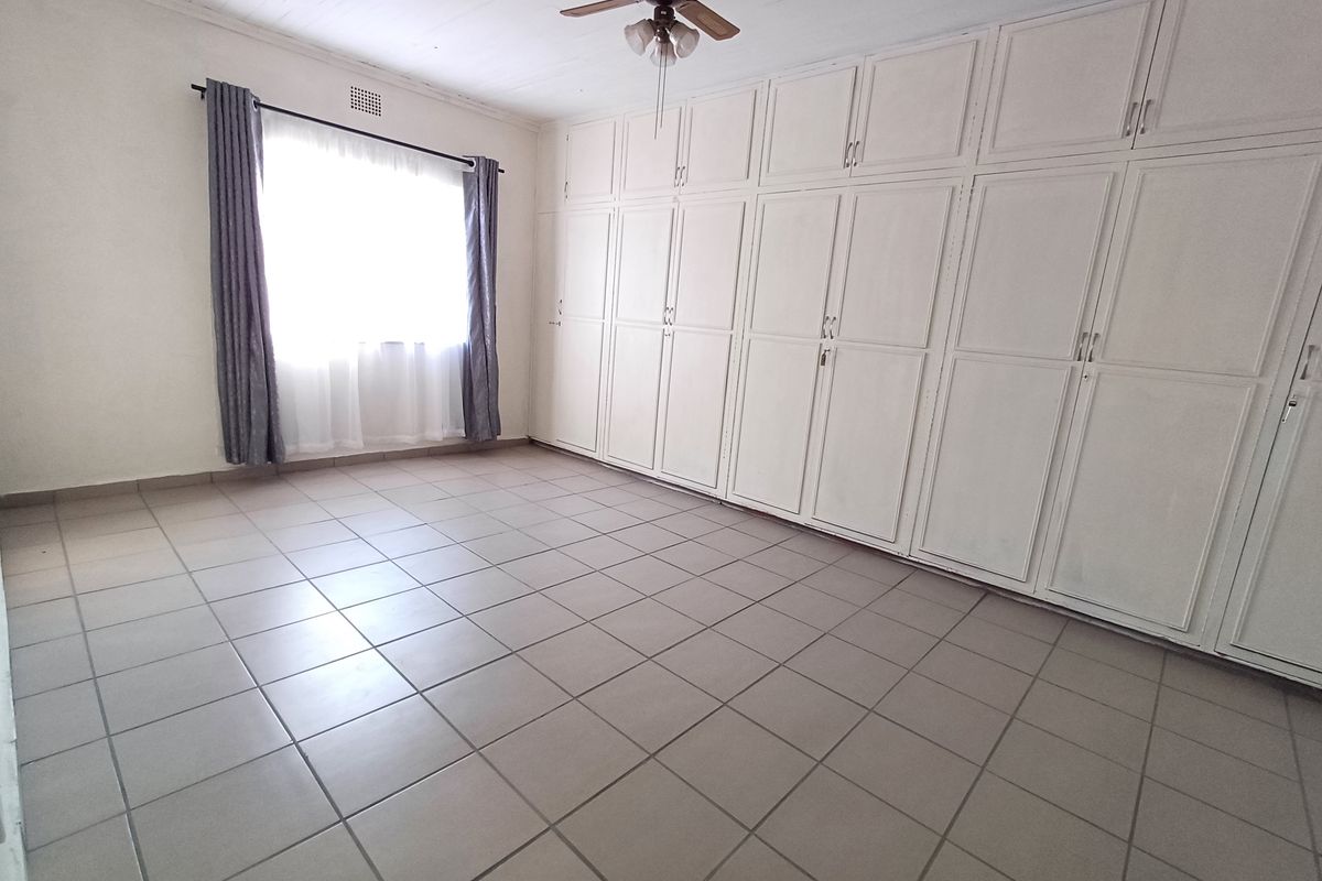 Spacious bedroom featuring extensive built-in storage, tiled flooring, and a ceiling fan, offering a clean and functional living space.