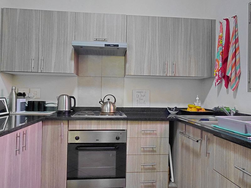 A functional kitchen featuring modern wood-grain cabinetry, granite countertops, a built-in oven with hob, and an extractor fan.