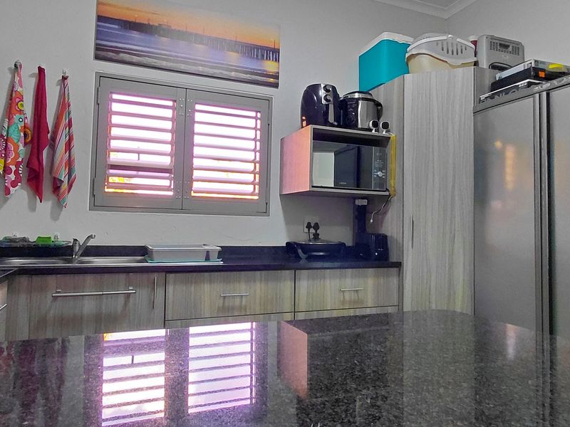 Functional kitchen featuring granite countertops, laminate cabinetry, built-in microwave shelf, and a stainless steel sink with a louvre window.