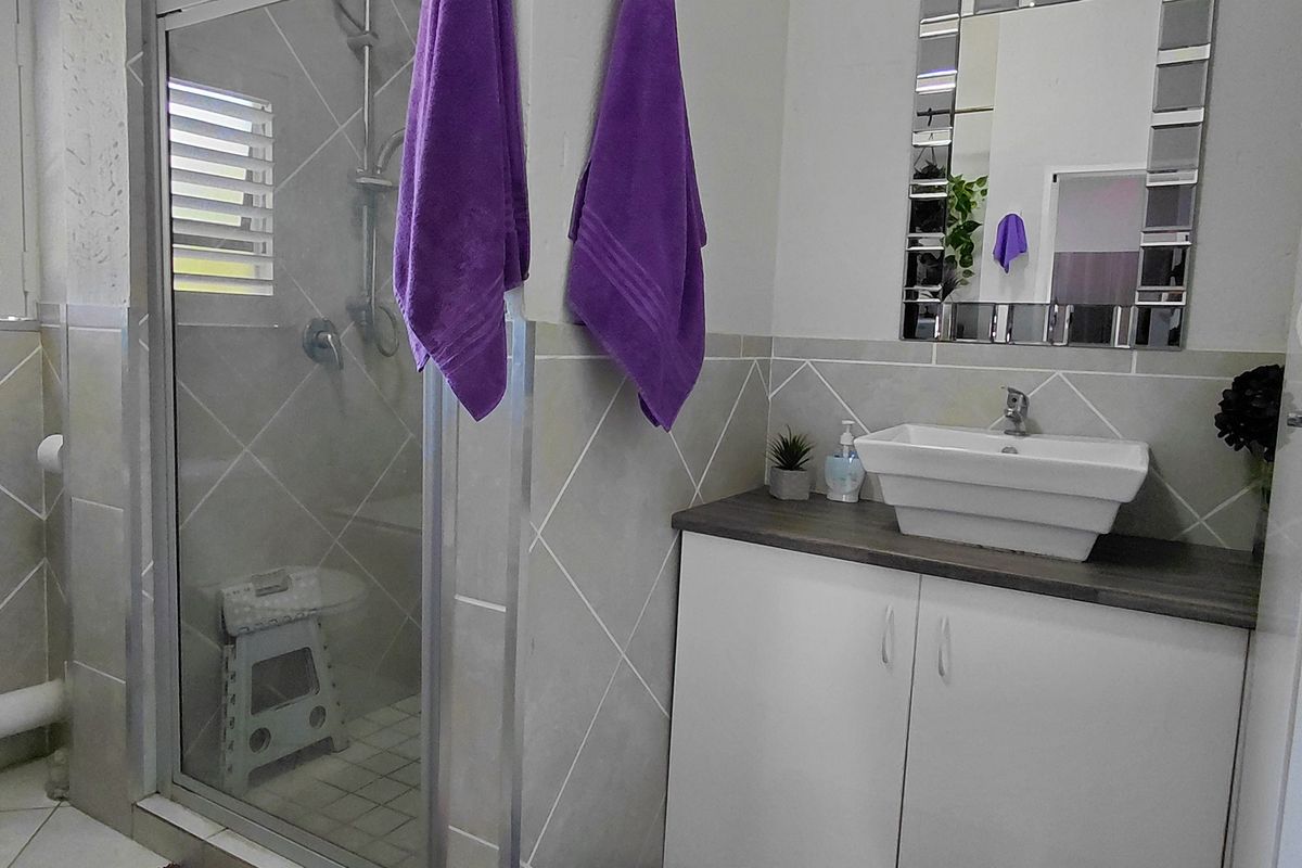 A functional bathroom featuring a glass-enclosed shower, a modern vessel sink with vanity storage, a toilet, and neutral wall tiling.