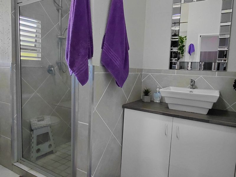 A functional bathroom featuring a glass-enclosed shower, a modern vessel sink with vanity storage, a toilet, and neutral wall tiling.