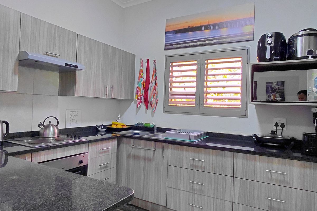 A functional kitchen featuring modern light wood-grain cabinetry, dark granite countertops, built-in oven, electric hob, and a louvered window for natural ventilation.
