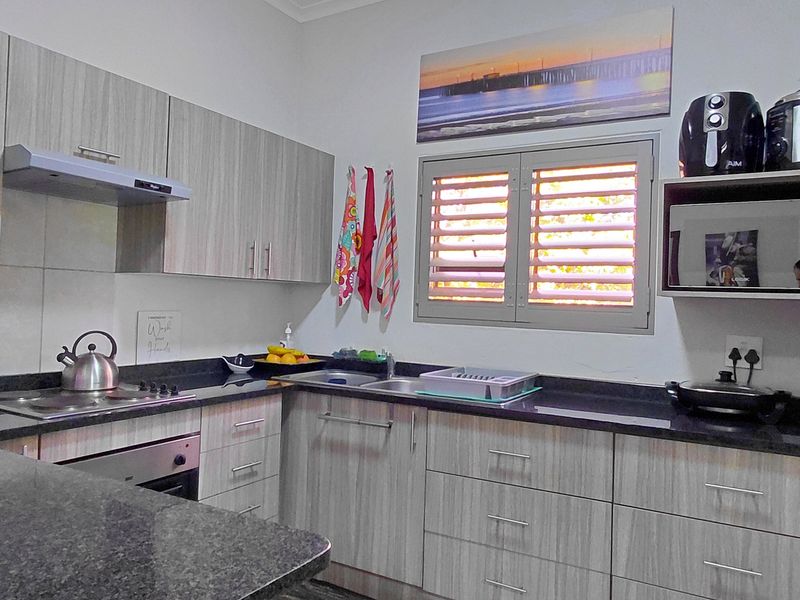 A functional kitchen featuring modern light wood-grain cabinetry, dark granite countertops, built-in oven, electric hob, and a louvered window for natural ventilation.