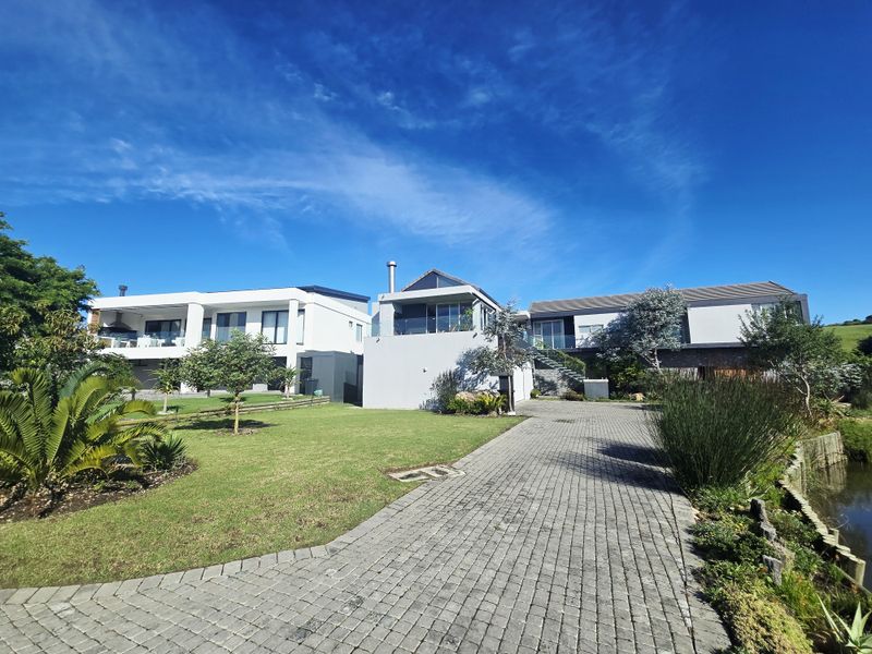 A modern multi-level residential property featuring a paved driveway, landscaped garden, and contemporary architectural design with glass balustrades.