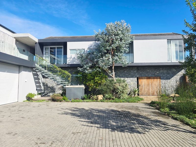 Modern double-story residence featuring stone cladding, a paved driveway, a glass-railed staircase, and a spacious garage.