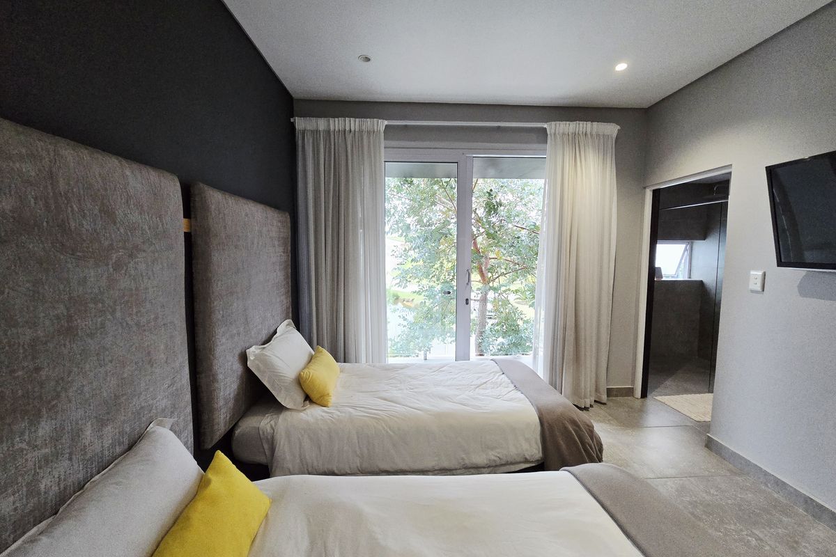 A modern bedroom featuring tiled floors, recessed lighting, and a sliding glass door providing natural light and garden views.