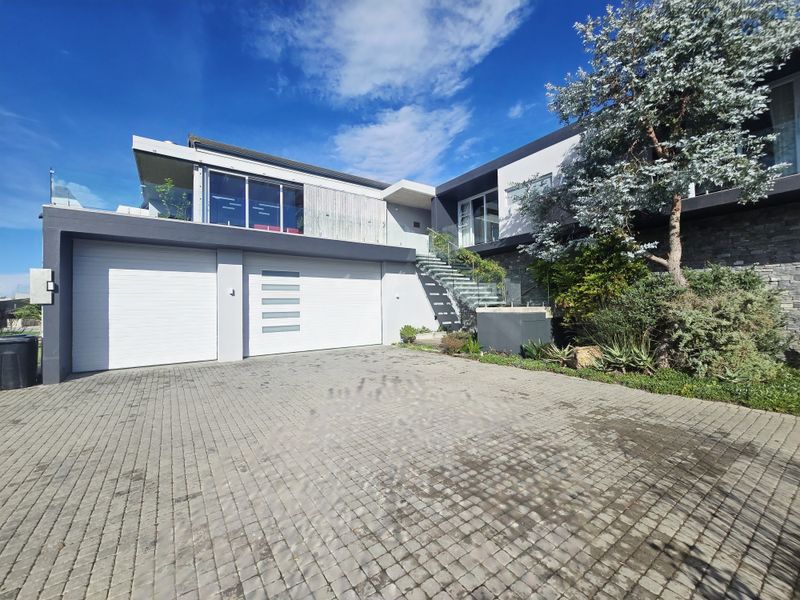 Modern double-story home featuring a paved driveway, double garage, stone cladding accents, and an external staircase leading to the upper level.