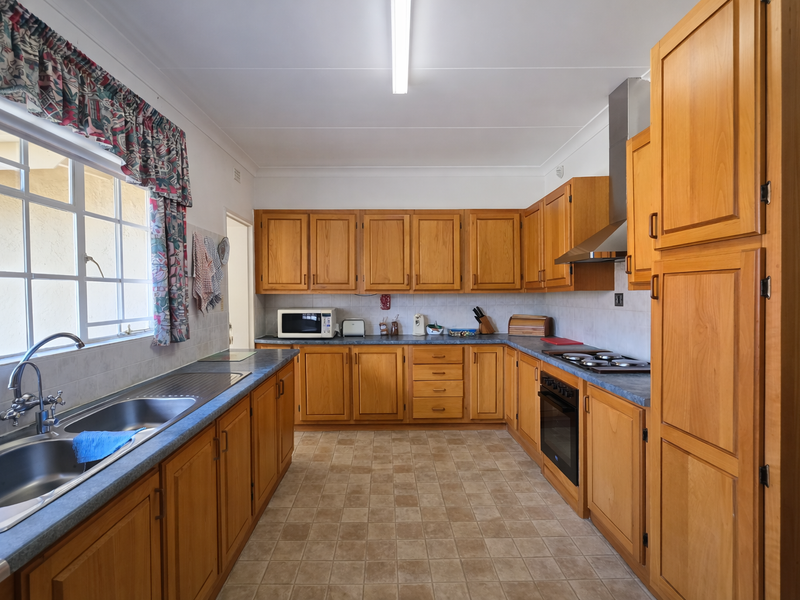 A functional kitchen featuring traditional wooden cabinetry, laminate countertops, a built-in oven and hob, and tiled flooring with ample storage space.