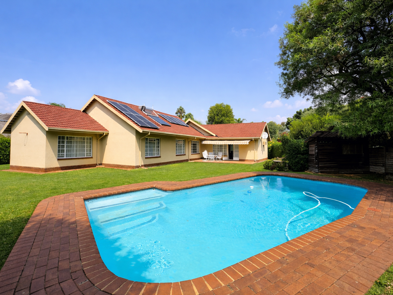 Rear view of the property featuring a well-maintained swimming pool, brick paved surround, solar panels on the tiled roof, and a spacious garden.