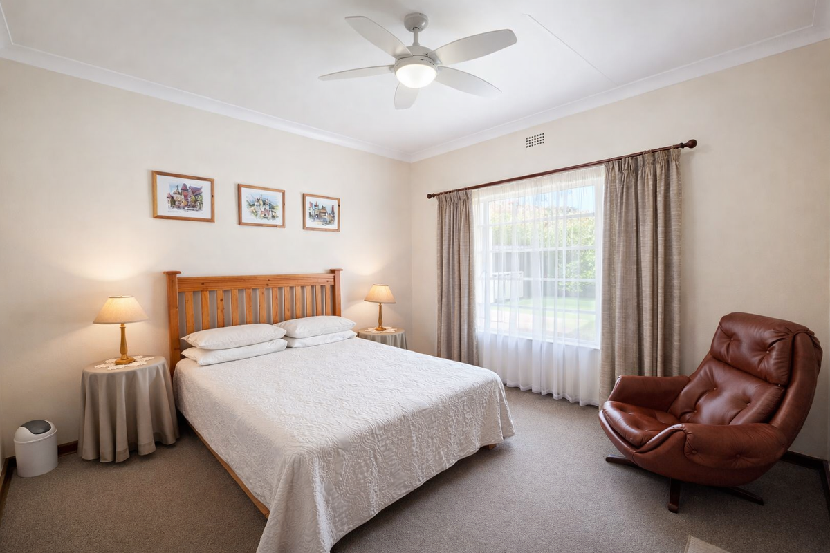 A well-maintained bedroom featuring neutral walls, carpeted flooring, a ceiling fan, and a large window providing natural light.
