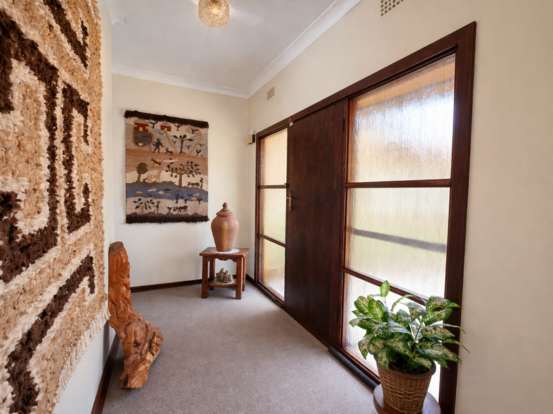 A bright entrance hall featuring a timber-framed glass door with textured glass panels, neutral walls, and carpeted flooring.