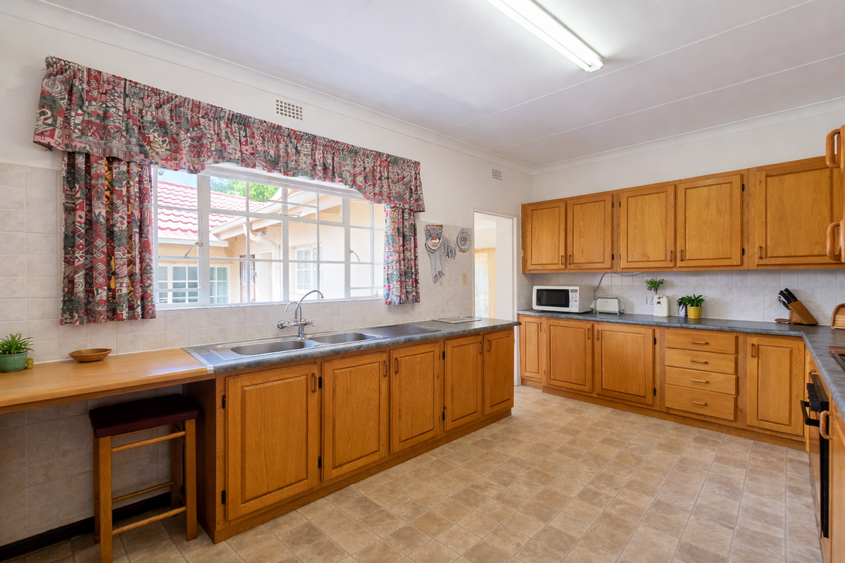 A spacious kitchen featuring traditional wooden cabinetry, laminate countertops, a double basin sink, and tiled backsplash, offering a functional layout with ample storage.