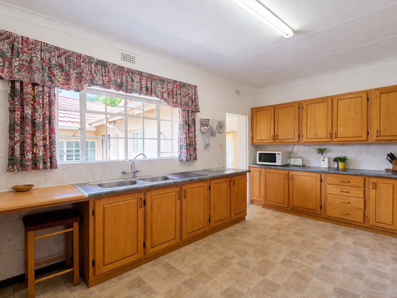 A spacious kitchen featuring traditional wooden cabinetry, laminate countertops, a double basin sink, and tiled backsplash, offering a functional layout with ample storage.