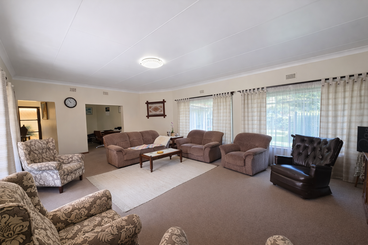 Spacious living room featuring neutral carpeting, large windows with curtain tracks, and classic ceiling coving, offering a comfortable and well-lit area.