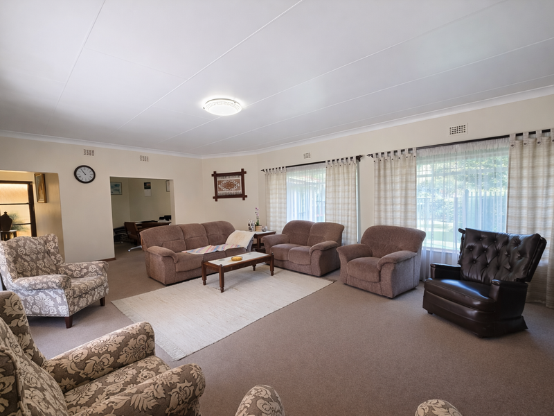Spacious living room featuring neutral carpeting, large windows with curtain tracks, and classic ceiling coving, offering a comfortable and well-lit area.