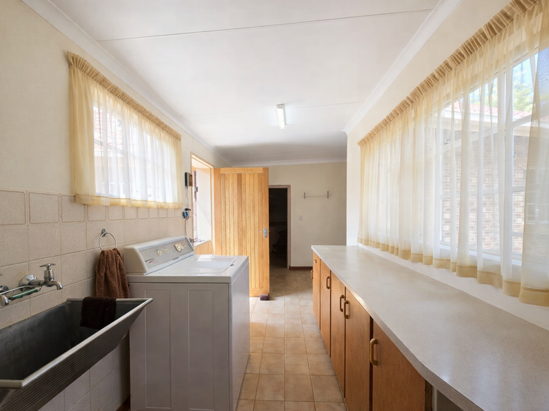 A functional laundry room featuring built-in cabinetry, laminate countertops, a stainless steel trough, and tiled flooring with ample natural light.