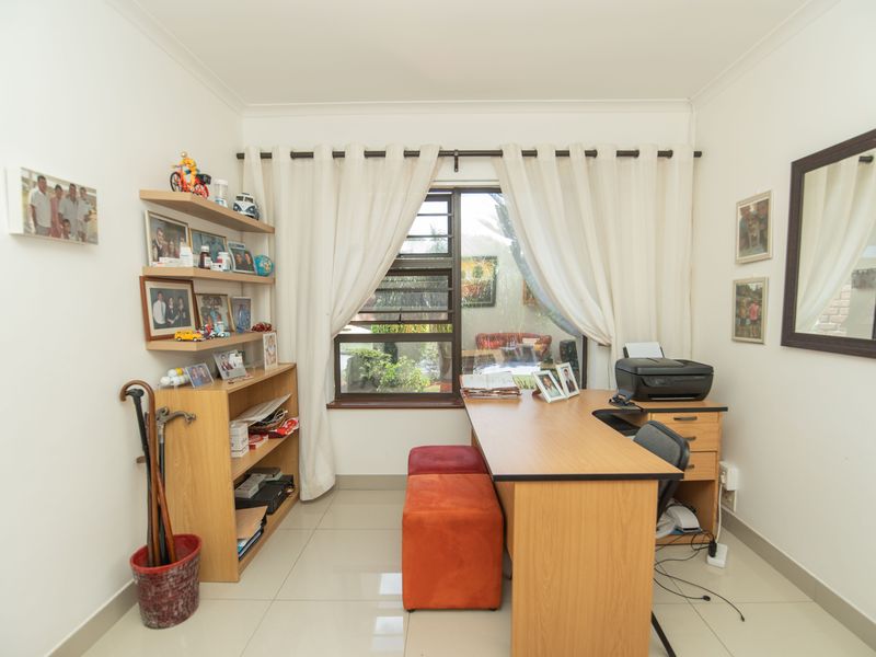 A functional home office space featuring tiled flooring and a large window with natural light, suitable for a dedicated workspace.
