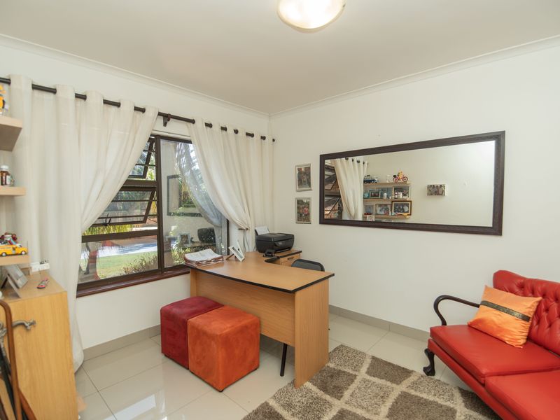 A bright home office featuring tiled flooring, a large window with natural light, and neutral wall finishes.