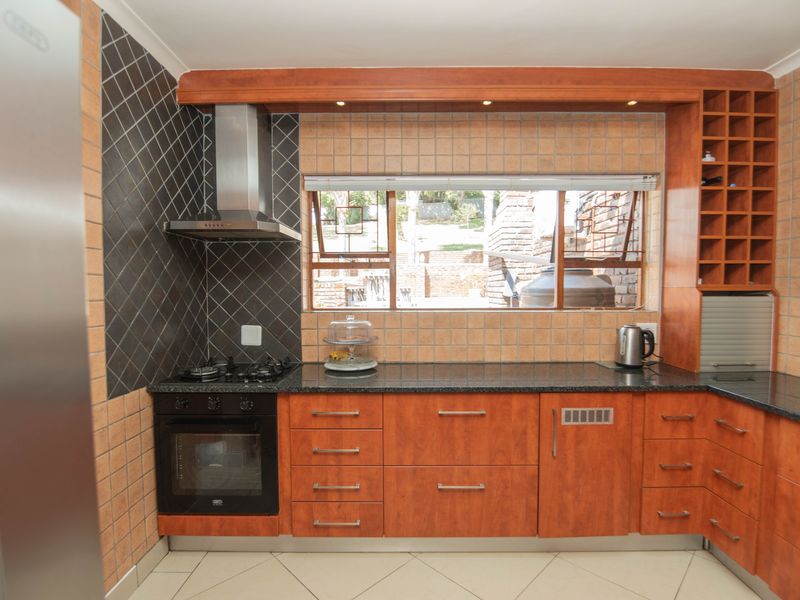 A functional kitchen featuring wooden cabinetry, granite countertops, a built-in oven with gas hob, and a tiled backsplash with a window overlooking the garden.