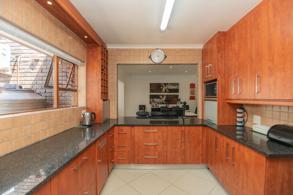 A functional kitchen featuring warm-toned wooden cabinetry, dark granite countertops, and a tiled backsplash, with an open-plan layout connecting to the dining area.