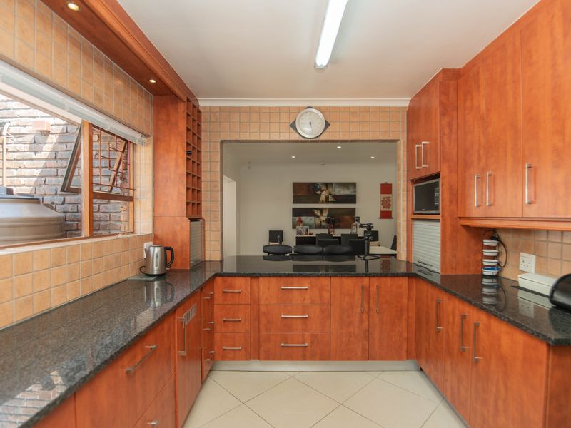 A functional kitchen featuring warm-toned wooden cabinetry, dark granite countertops, and a tiled backsplash, with an open-plan layout connecting to the dining area.