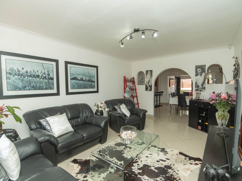 Spacious open-plan living area featuring neutral tiled flooring, an elegant archway leading to the dining space, and modern track lighting.