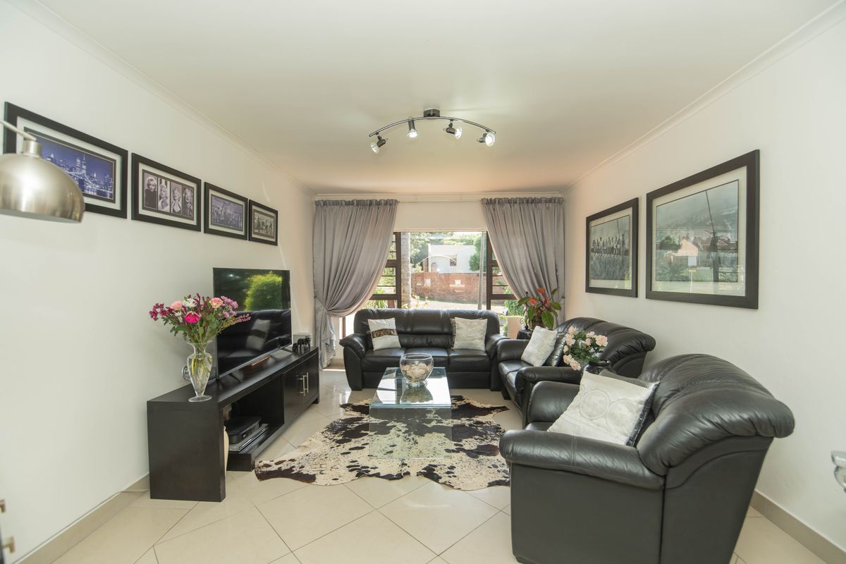 A well-maintained living room featuring neutral tiled flooring, cove cornicing, and modern track lighting, providing a comfortable and functional space.