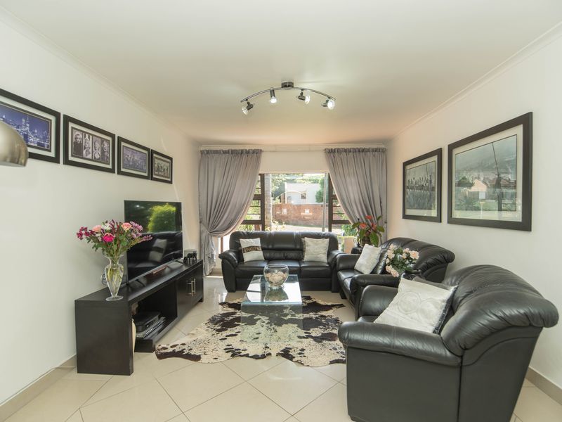 A well-maintained living room featuring neutral tiled flooring, cove cornicing, and modern track lighting, providing a comfortable and functional space.
