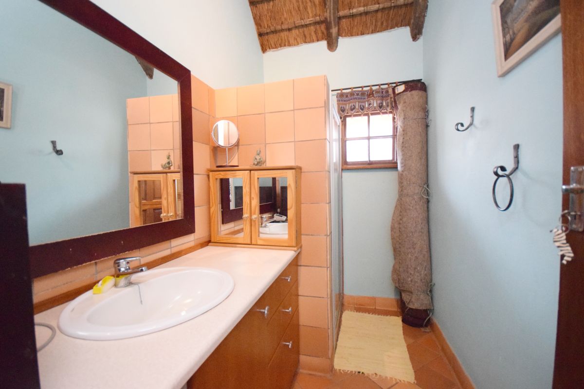 A bathroom featuring a vanity with a basin, tiled splashback, shower enclosure, and a traditional thatched roof ceiling.